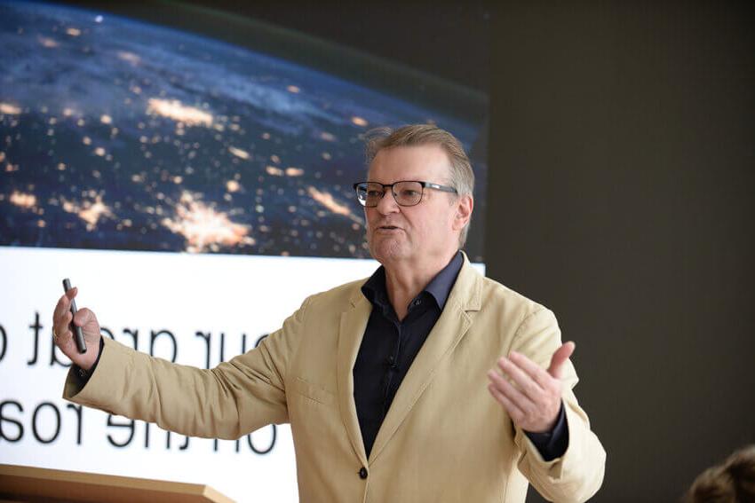 Antony Slumbers, in a tan suit and dark shirt, gesturing in front of a presention slide at a Mitie Estate Optimisation event