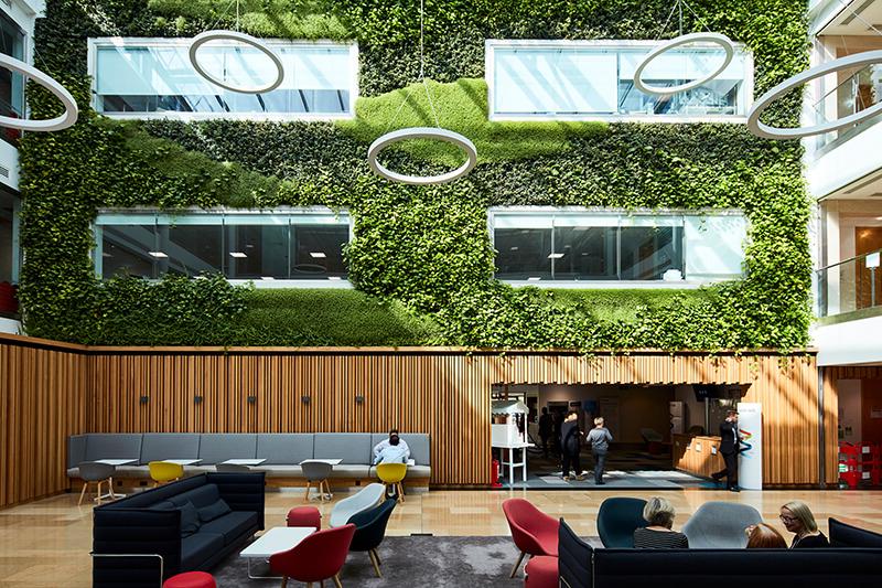 Modern open-plan office reception space with sofas and chairs and a green living wall on the upper levels